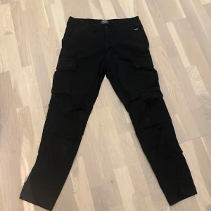 Svarta cargopants med fickor - Snygga svarta cargopants med flera praktiska fickor på sidorna. Perfekta för en avslappnad stil och passar bra till vardags. Byxorna har en normal passform och är tillverkade i ett slitstarkt material.