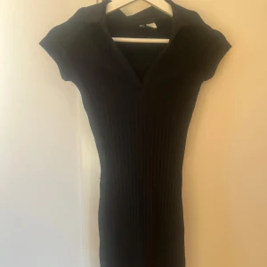 Svart ribbad klänning från H&M - Snygg svart ribbad klänning med v-ringning och korta ärmar. Perfekt för en stilren look. Klänningen har en figurnära passform som framhäver silhuetten.