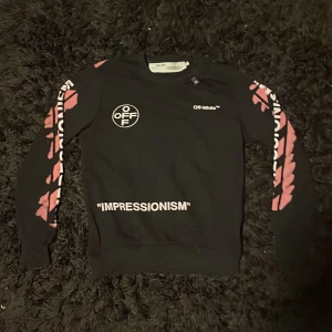  Off White hoodie - Säljer en svart tröja från Off-White med tryck i rosa och vitt. Tröjan har långa ärmar med texten 'IMPRESSIONISM' och ett stort grafiskt tryck på baksidan. Perfekt för dig som vill ha en skön tröja till sommaren. Scan finns. Hör av dig om du jag några funderingar