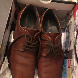 Bruna skinnloafers från Memphis One - Säljer ett par klassiska bruna loafers från Memphis One i skinn med snörning och rund tå. Perfekta för en stilren look och passar till många olika outfits. Snygga sömmar och bekväm platt sula.