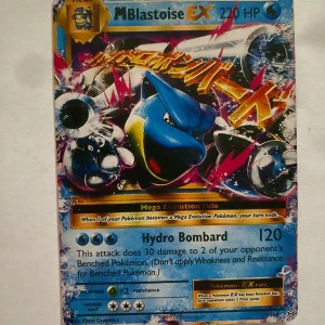 Pokémonkort M Blastoise EX - Säljer ett samlarkort från Pokémon, M Blastoise EX med 220 HP från serien Evolutions. Kortet har en färgstark design med Blastoise i blått och silver, samt attacken Hydro Bombard. Perfekt  för samlare eller Pokémon-fans! Kortet är värderat till 21 dollar vilket motsvarar ungefär 210kr.