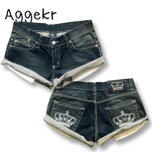 Minishorts från Victoria Beckham - Snygga mörkblå jeansshorts med upprullade benslut och vita sömmar. Baksidan har broderade kronor på fickorna och en liten patch upptill. Klassisk femficksmodell med knapp och dragkedja framtill.
