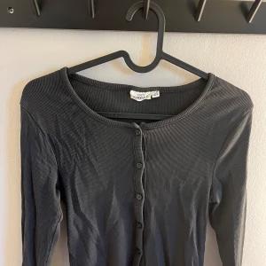 Grå ribbad kofta - Säljer en stilren grå ribbad kofta med knappar framtill. Koftan har långa ärmar och en croppad design med vågiga kanter. Perfekt för lager-på-lager-stil. Från Kappahl i storlek 158/164. Använd ett fåtal gånger💓
