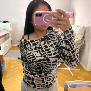 Svartvit långärmad tröja med grafiskt mönster - Säljer en svartvit långärmad tröja med ett unikt grafiskt rutmönster. Är i ett stretchigt material som sitter tight mot kroppen. Perfekt för dig som vill sticka ut med en cool och modern stil.