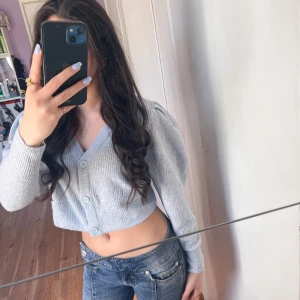 Ljusblå croppad kofta från H&M Divided - Säljer en ljusblå, croppad kofta från H&M Divided. Koftan har v-ringning, långa ärmar och knappar framtill. Den är stickad i mjukt material och passar perfekt till jeans eller kjol.