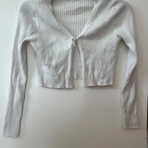 Vit ribbad croppad kofta från Primark - Säljer en vit ribbad kofta från Primark köpte Paris. Tröjan är croppad, har långa ärmar och knytning framtill. Perfekt att slänga över en topp för en enkel och stilren look.