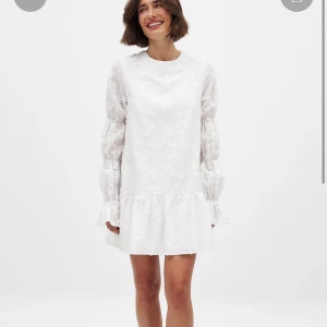 Studentklänning - Superfin vit kortklänning från nakd med blommigt broderi, volang nertill och långa puffärmar. Klänningen har öppen rygg med knytband. Perfekt för studenten! Aldrig använd och prislapp kvar💕nypris 699