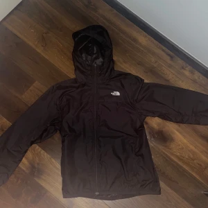 North Face windbreaker  - Säljer en svart vindjacka från The North Face med huva och dragkedja framtill. Jackan har en klassisk passform och är perfekt för blåsiga dagar. Logotypen syns både fram och bak på jackan.