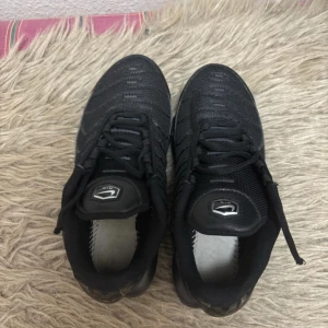 Svarta Nike Air Max sneakers - Säljer ett par helsvarta Nike Air Max sneakers med synlig luftbubbla i sulan och diskret Nike-logga på sidan. Skorna har snörning och är tillverkade i en kombination av mesh och syntetmaterial för en sportig look.