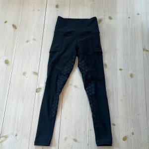 Svarta ridleggings från Maya Delorez - Svarta ridleggings från Maya Delorez med hög midja och smarta fickor på sidorna. Snygga detaljer med silikonmönster på insidan av benen för extra grepp. Perfekta för dig som vill ha både stil och funktion i stallet.