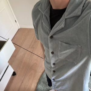 Ljusblå kortärmad skjorta med bröstficka i frotté från studio total  - Säljer en ljusgrå kortärmad skjorta i frotté med klassisk krage och knäppning framtill. Perfekt för en avslappnad stil. Storlek M 