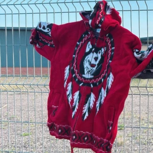 Röd stickad hoodie med vargmotiv - Röd stickad zip hoodie med stort vargmotiv. Tröjan har huva och långa ärmar. 