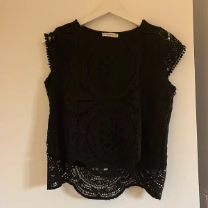 Svart spetsblus med kort ärm - Säljer en svart blus i spets med vackra detaljer och korta ärmar. Står storlek M men passar perfekt för S och Xs oxå❣️