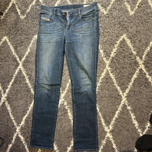 Blå jeansbyxor från Diesel - Snygga blå jeansbyxor från Diesel med klassisk femficksdesign och raka ben. Byxorna har en liten Diesel-logga vid fickan fram och en patch bak i midjan. Perfekta för en avslappnad och stilren look.