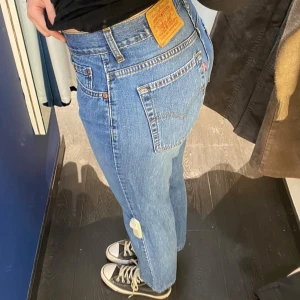 Levis 501 blå jeans - Klassiska blå Levis 501 jeans med rak passform och knappgylf. Jeansen har en bakficka med Levis-röd etikett och läderpatch i midjan.
