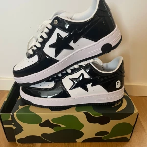Svarta och vita Bape Sta sneakers - Säljer ett par Bape Sta sneakers i svart och vitt med glansig finish. Skorna har den klassiska stjärndetaljen på sidan, vit sula och svarta detaljer. Perfekta för dig som gillar streetwear och vill sticka ut med en ikonisk modell.