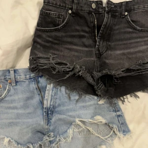 Två par jeansshorts med fransar - Säljer två par jeansshorts, ett par i ljusblå denim och ett par i sorte denim. Båda har råa, fransiga kanter och slitna detaljer för en cool, avslappnad look. Perfekta för sommaren och festivaler. Kan købes hver for sig