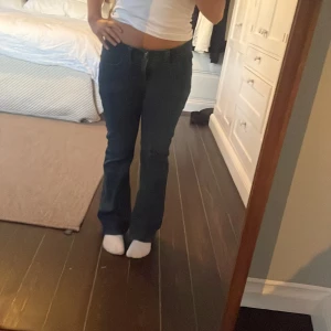 Mörkblå bootcut jeans med broderad bakficka - Säljer ett par mörkblå Lee jeans med bootcut passform och snyggt broderad detalj på bakfickan. Jeansen är lågmidjade och har klassisk femficksdesign. Perfekta för en avslappnad och trendig look.