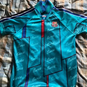 Turkos FC Barcelona retro fotbollströja - Säljer nu denna feta retro FC Barcelona tröjan med en krage. Tröjan är bra skick och har inte kommit till användning så mycket. Inga tecken på hål,fläckar eller annat dåligt. Köpte den i Barcelonas shop i Barcelona för drygt 900kr på höstlovet 2024. Sälj då den är för liten. Strolek S men passar även M. Kom PM för frågor, finns inga dumma frågor. Priset är ej hugget i sten.