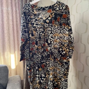 Mönstrad långärmad klänning - Säljer en långärmad klänning med färgstarkt mönster i svart, vit, orange och beige. Klänningen har lös passform och är perfekt för dig som gillar unika prints. Rund halsringning och mjukt material. Passar dig med storlek 46-48