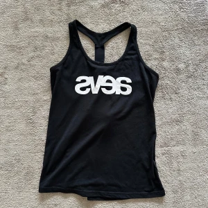 Svart träningstopp - Svea - Svart träningstopp med brottarygg och en snygg öppen detalj på ryggen. Perfekt för gymmet eller andra träningspass.