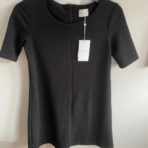 Svart kortklänning från Vila - Säljer en svart kortklänning från Vila i storlek XS. Klänningen har rund halsringning, korta ärmar och en diskret struktur i tyget. Enkel och stilren modell som passar perfekt till många tillfällen.