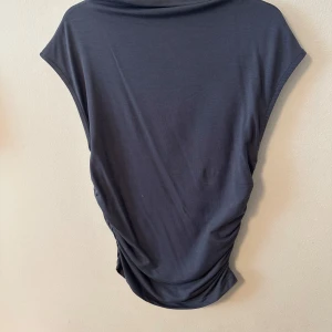 Mörkgrå topp från Gina Tricot - Säljer en mörkgrå topp från Gina Tricot i storlek XS. Toppen har en tajt  passform med korta ärmar och är tillverkad i ett mjukt, stretchigt material. 