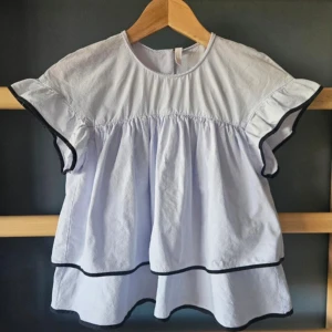 Ljusblå volangblus med svarta kanter från Zara - Superfin ljusblå blus från Zara med volanger och knappar i ryggen. Perfekt till  vår och sommar🌺Inte alls använd så mkt så är i super skickt☺️