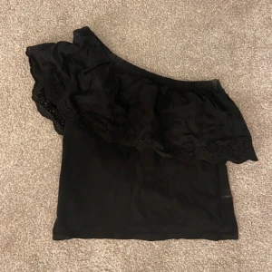 Svart oneshoulder topp med volang - Säljer en svart volang oneshoulder topp köpt i Spanien! Jättefint mönster. Endast testad. Perfekt på sommaren💘