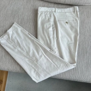 Beige kostymbyxor med pressveck - Snygga beige kostymbyxor med klassiskt snitt och pressveck. Byxorna har fickor fram och bak, samt stängs med knapp och dragkedja. Perfekta för en dressad look.