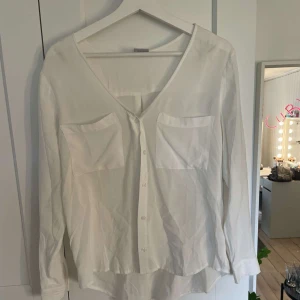 Vit blus med v-ringning från Cubus  - Säljer en stilren vit blus från Cubus med v-ringning och två bröstfickor. Blusen har knappar framtill och långa ärmar. Perfekt för en clean och enkel look. Storlek 36💗 Använd inte köp nu! 