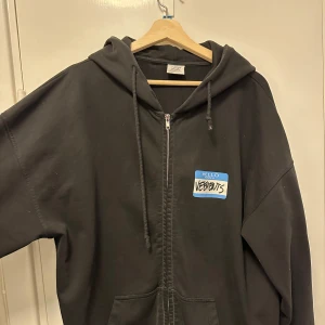 Vetements  - Svart oversized hoodie från Vetements med dragkedja framtill och huva. Stor blåvit etikett med texten 'Hello my name is Vetements' på både fram- och baksida. Broderad text 'Vetements Limited Edition' på ärmen. Perfekt statement-plagg.