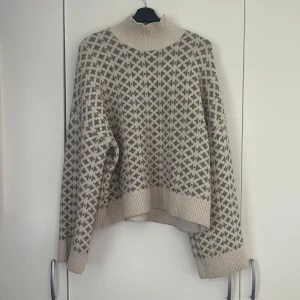 Beige stickad polotröja från Lindex  - Mysig beige stickad polotröja med grått geometriskt mönster. Tröjan har långa vida ärmar! Storlek M