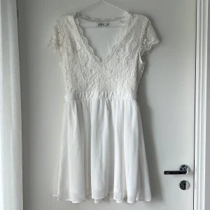 Vit spetsklänning från NLY One - Superfin vit kortklänning från NLY One med spets upptill och v-ringning. Kjolen är lätt och flowy, medan överdelen har vackra spetsdetaljer och korta ärmar. Perfekt för sommarens alla tillfällen eller studentfirande!