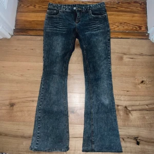 Bootcut jeans i tvättad blå denim - Snygga bootcut jeans i tvättad blå denim med slitna detaljer och klassisk femficksmodell. Jeansen har en lätt utsvängd passform nertill och coolt tryck på bakfickorna. Perfekta för dig som gillar en retro vibe och vill sticka ut lite extra. En defekt som syns på sista bilden.