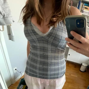Grå rutig halternecktopp med spets - Supersnygg grå och blå rutig korsettopp med v-ringning och spetskant. Toppen har knappar framtill, bälte i midjan och är ärmlös med smala axelband. Perfekt för dig som gillar en tight och trendig look. Storleken står inte men gissar S/M