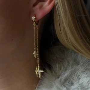 Guldiga örhängen med stjärndetaljer - Snygga guldiga örhängen med långa kedjor och glittrande stjärn- och diamantformade hängen. Perfekt för dig som vill sticka ut med coola detaljer och elegant vibe. Kedjorna ger ett trendigt och unikt intryck.