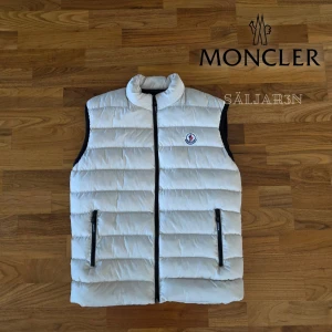 Vit Moncler Väst - Letar du efter en stilren väst som kombinerar lyx och funktion? Denna Moncler-väst i vitt (storlek S) är i nyskick och perfekt för lager-på-lager eller som lätt ytterplagg. Tillverkad i slitstarkt nylon med dunfyllning. Broderad logga, innerfoder med serietryck och dragkedjefickor. Passar både till vardag och mer uppklätt.  📦 Snabb leverans – skickas samma dag vid köp! 📦 Hör av dig vid intresse eller om du har frågor!📌 #moncler #lyxmode #herrmode  
