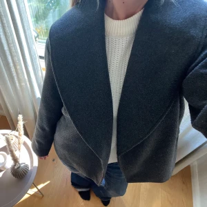 Mörkgrå kappa - Säljer en stilren mörkgrå kappa i ull med bred, snygg krage och rak passform. Perfekt till hösten!!