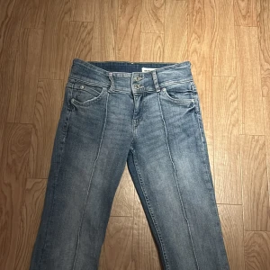 Blå bootcut jeans från Bershka - Snygga blå jeans från Bershka i bootcut-modell med markerad söm längs benen. Klassisk femficksdesign, låg midja och lätt slitning för en cool vintagekänsla. Perfekta för dig som gillar en avslappnad men trendig look.