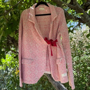 Rosa och vit mönstrad kofta med knyt - Superfin kofta från Odd Molly i stickad bomull med rosa och vitt mönster. Koftan har lång ärm, två fickor fram och en snygg röd rosett som knytning i midjan. Perfekt för dig som gillar detaljer och vill ha en mysig, unik look. Storlek 3 som enligt deras storleksguide motsvarar en storlek L. Mer använd, finns små anmärkningar se bilder. Kan förekomma lösa trådar på insidan. 