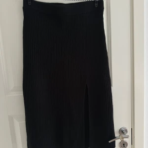 Svart ribbad långkjol från NLY Trend - Svart ribbstickad långkjol från NLY Trend med snygg slits framtill. Kjolen har en tight passform och är gjord i ett stickat material som känns både mjukt och följsamt. Perfekt för dig som gillar en stilren och enkel look.