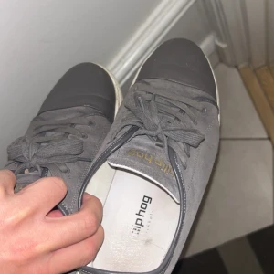 Grå sneakers från Philip Hog mocka - Snygga grå sneakers från Philip Hog med ovandel i mocka och tåparti i mörkare grått skinn. Skorna har klassisk snörning, vit sula och diskret guldfärgad logga på plösen. Perfekta för en stilren och avslappnad look.