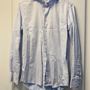 Ljusblå skjorta från Stenströms - Snygg ljusblå skjorta från Stenströms med diskret randigt mönster. Tillverkad i exklusiv tvåfaldig bomull, har klassisk krage, långa ärmar med dubbla manschettknappar och knappar framtill. Perfekt för dig som gillar stilrena och fräscha plagg.