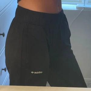 Svarta mjukisbyxor från Adidas - Svarta mjukisbyxor från Adidas med klassisk logga på benet. Byxorna har resår i midjan, smal passform och muddar vid bensluten. Perfekta för chill eller träning, med mjukt material och fickor på sidorna.
