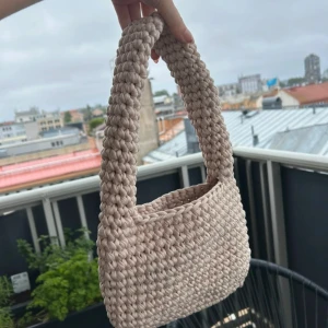 Virkad väska - Hemmavirkad beige väska i 100% t-shirtgarn i överskott från textilindustrin. Väskan är 24cm bred, 16cm hög och 36cm hög inklusive handtag. Aldrig använd