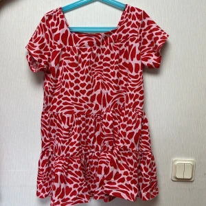 Röd och vit hjärtmönstrad kortklänning - Säljer en söt kortklänning med hjärtmönster i rött och vitt. Klänningen har volanger nertill, korta ärmar och en fyrkantig ringning. Perfekt för dig som gillar färgglada och lekfulla plagg. Materialet känns lätt och luftigt.
