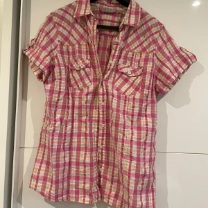 Rutig rosa kortärmad skjorta - Snygg rutig skjorta från Cappuccino i rosa, vit och gul. Modellen har korta ärmar med knappdetalj, klassisk krage och två bröstfickor. 