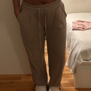 Beige mjukisbyxor med snörning - Säljer ett par beige mjukisbyxor med bred resår i midjan och snörning framtill. Byxorna har raka ben, stora fickor fram och bak samt är tillverkade i mjukt material som känns skönt mot huden. Perfekta för chill dagar hemma eller när du vill vara bekväm. Knappt använt dem, max 2-3 gånger. Anledning för att dem är för stora pga viktnedgång. 