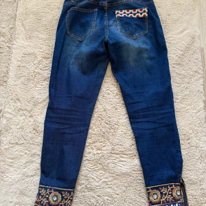 Desigual Exotic Jeans med brodyr - Unika blå jeans från Desigual med broderade detaljer längst ner på benen och färgglad brodyr på ena bakfickan. 